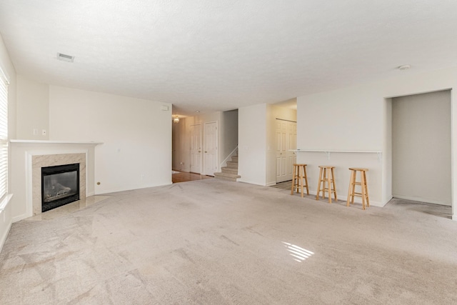 unfurnished living room featuring light carpet, a premium fireplace, a textured ceiling, and indoor bar