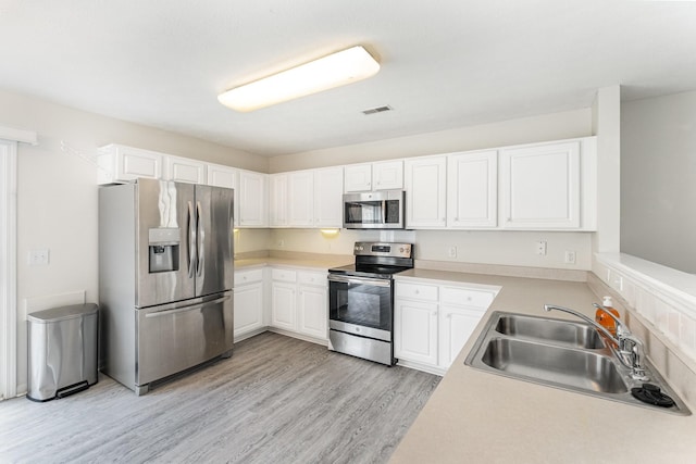 kitchen with appliances with stainless steel finishes, sink, white cabinets, and light hardwood / wood-style flooring