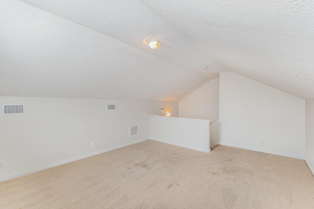 bonus room with lofted ceiling, light carpet, and a textured ceiling