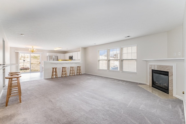 unfurnished living room with light colored carpet, a premium fireplace, and a chandelier