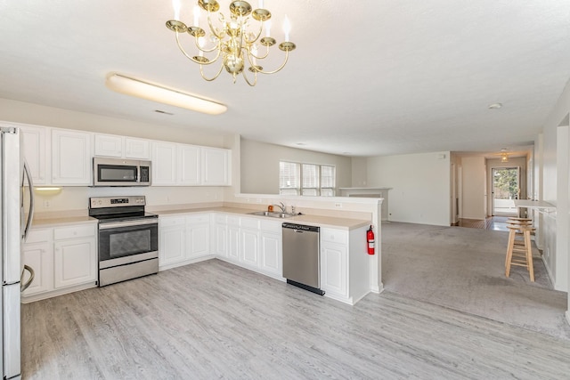 kitchen with decorative light fixtures, appliances with stainless steel finishes, kitchen peninsula, a wealth of natural light, and white cabinets