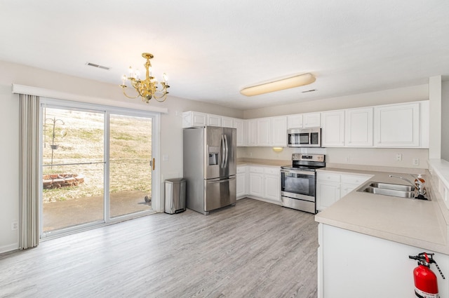 kitchen with sink, appliances with stainless steel finishes, white cabinetry, hanging light fixtures, and light hardwood / wood-style floors