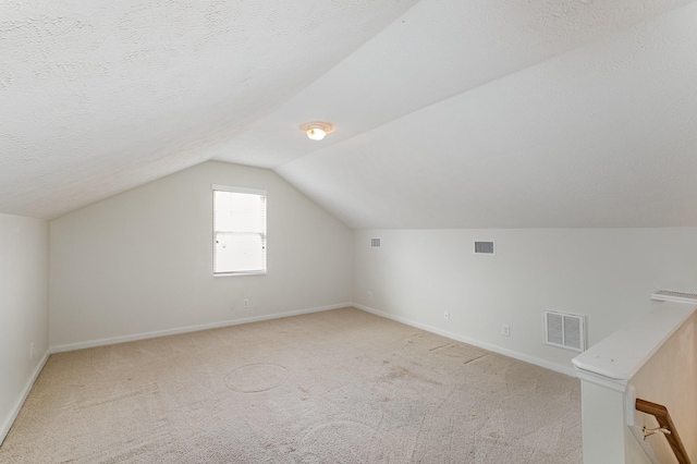 bonus room with lofted ceiling, light colored carpet, and a textured ceiling