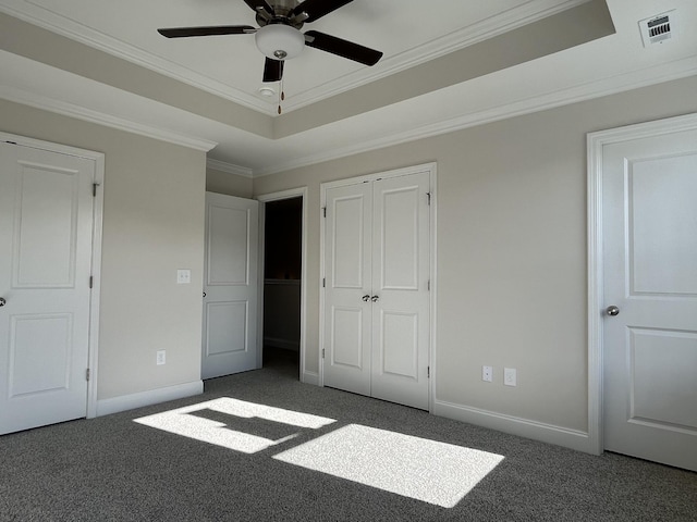 unfurnished bedroom featuring crown molding, a closet, dark carpet, and a tray ceiling