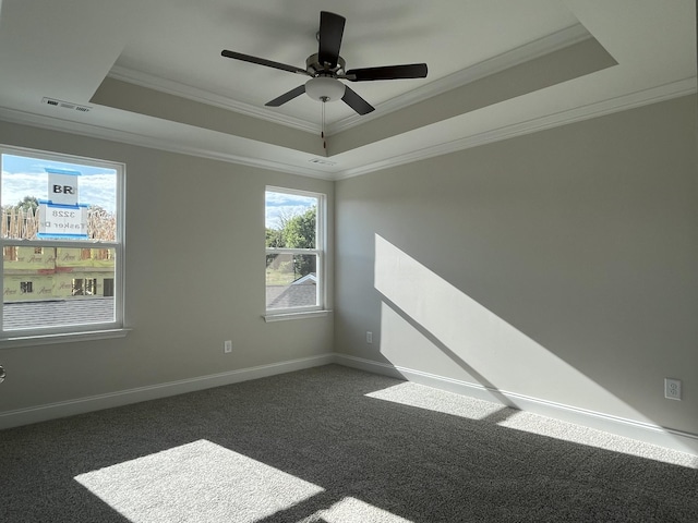 empty room with crown molding, ceiling fan, a tray ceiling, and dark colored carpet