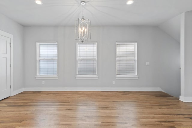 unfurnished dining area featuring lofted ceiling, hardwood / wood-style floors, and a notable chandelier