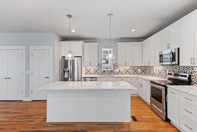 kitchen with a kitchen island, pendant lighting, white cabinets, stainless steel appliances, and light stone countertops