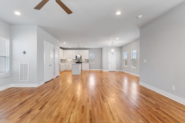 unfurnished living room featuring ceiling fan with notable chandelier and light hardwood / wood-style flooring