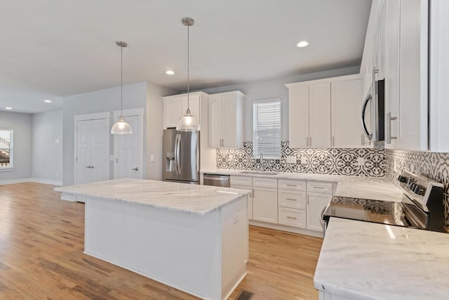 kitchen featuring appliances with stainless steel finishes, pendant lighting, white cabinetry, a center island, and light stone countertops