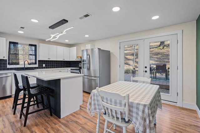 kitchen with a kitchen island, appliances with stainless steel finishes, pendant lighting, white cabinetry, and sink