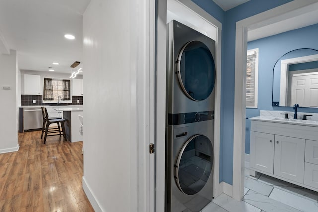 laundry area featuring stacked washer and clothes dryer, sink, and light wood-type flooring