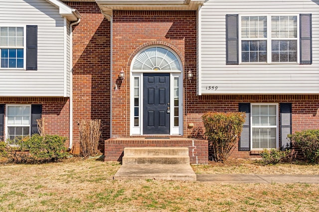 view of exterior entry with a yard and brick siding