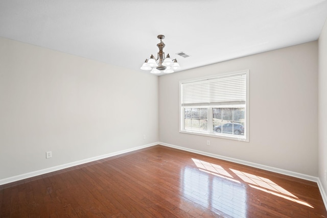 empty room featuring visible vents, a notable chandelier, baseboards, and wood finished floors