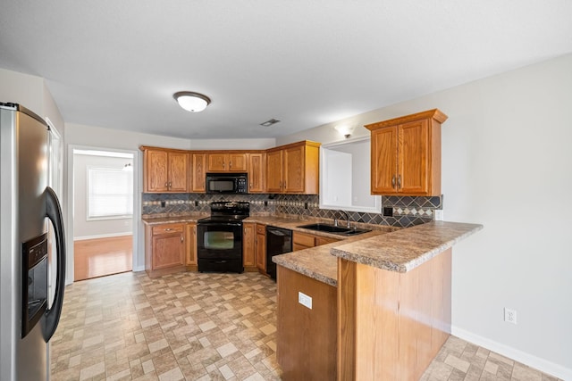 kitchen featuring a peninsula, black appliances, decorative backsplash, and a sink