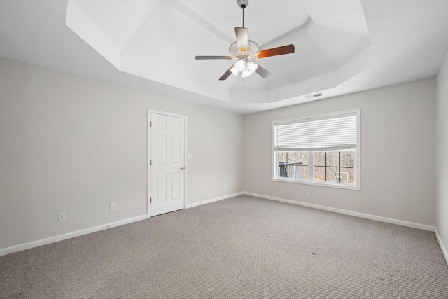 spare room featuring a tray ceiling, carpet flooring, visible vents, and baseboards