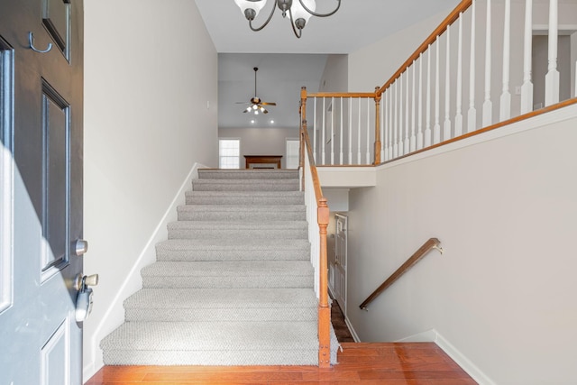 stairway featuring a high ceiling, wood finished floors, a ceiling fan, and baseboards