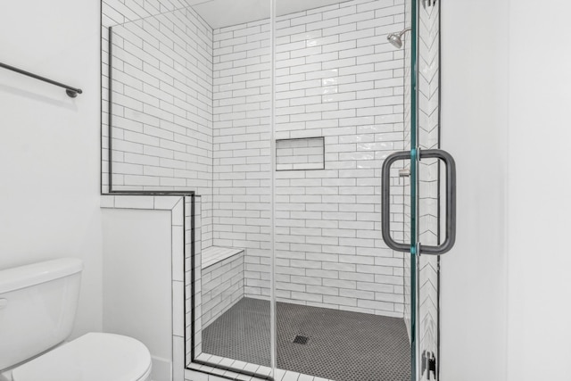 bathroom featuring a shower with shower door and toilet