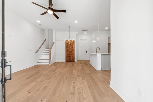 unfurnished living room featuring sink, ceiling fan with notable chandelier, and light wood-type flooring