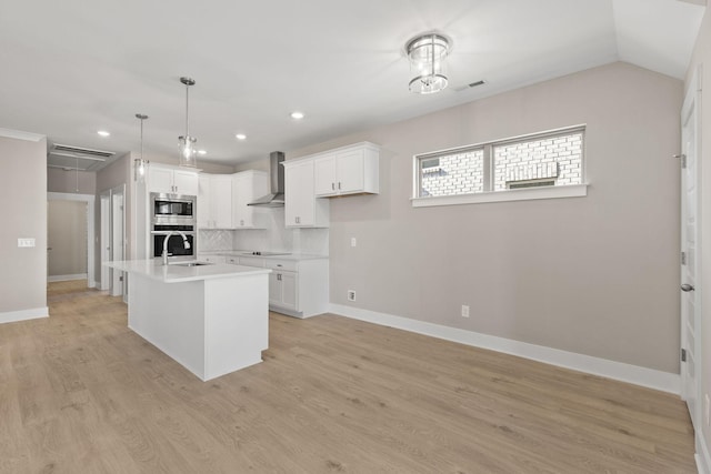 kitchen featuring wall chimney range hood, white cabinetry, stainless steel appliances, an island with sink, and decorative backsplash