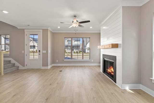 unfurnished living room with ornamental molding, a large fireplace, ceiling fan, and light wood-type flooring