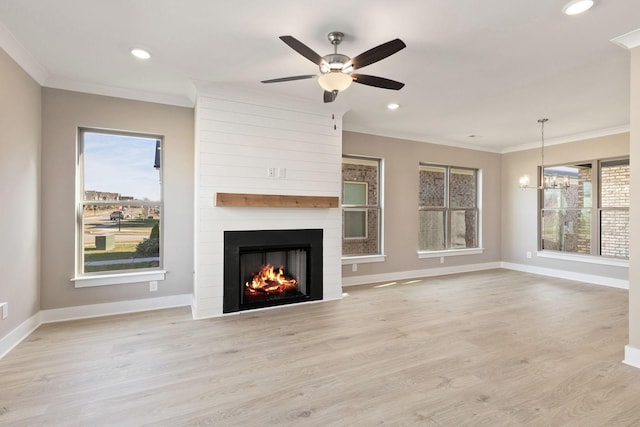 unfurnished living room featuring crown molding, light hardwood / wood-style flooring, a large fireplace, and ceiling fan with notable chandelier