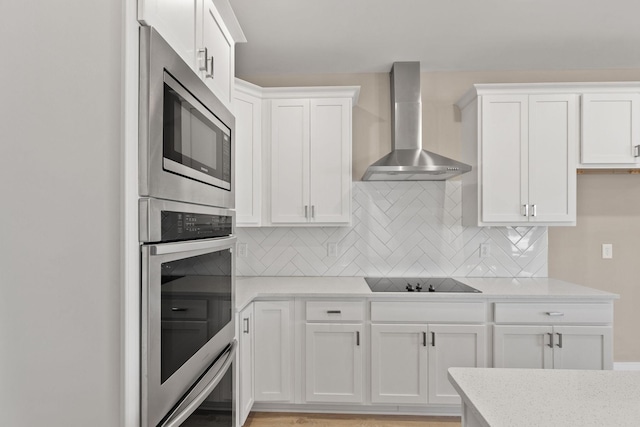 kitchen with white cabinetry, decorative backsplash, light stone counters, stainless steel appliances, and wall chimney exhaust hood