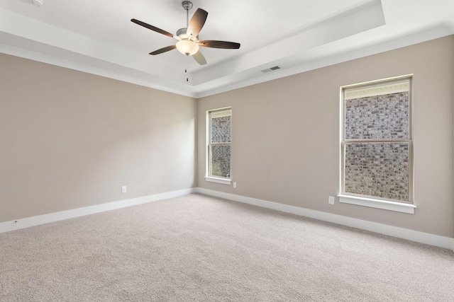 carpeted empty room featuring a raised ceiling, ornamental molding, and ceiling fan