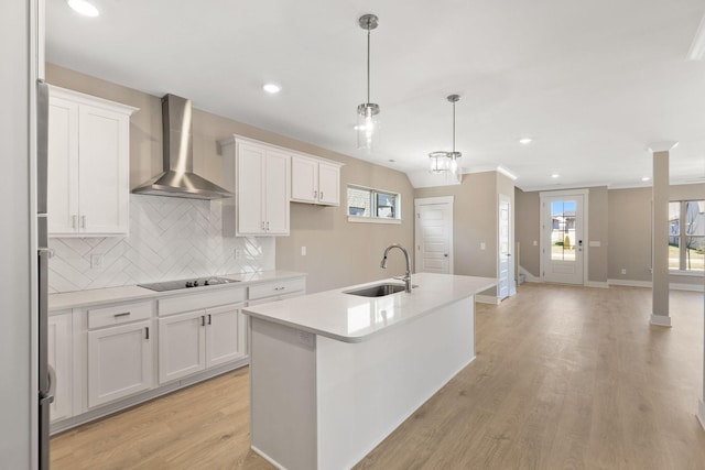 kitchen featuring a kitchen island with sink, white cabinets, decorative light fixtures, and wall chimney exhaust hood