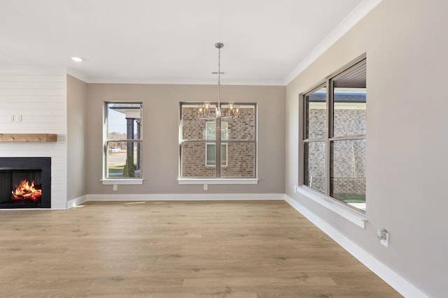 unfurnished dining area featuring crown molding, a notable chandelier, a fireplace, and light hardwood / wood-style flooring