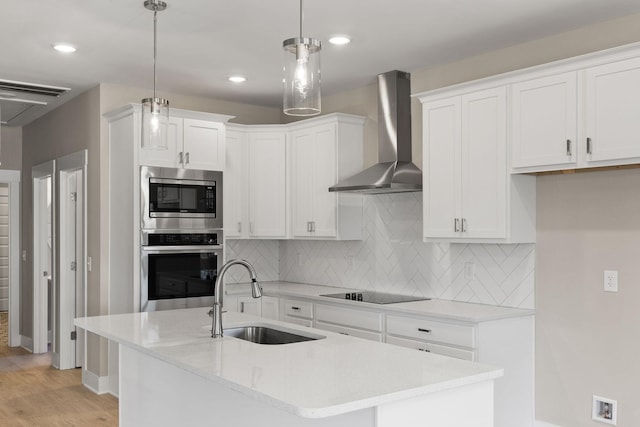 kitchen with pendant lighting, sink, white cabinetry, stainless steel appliances, and wall chimney exhaust hood