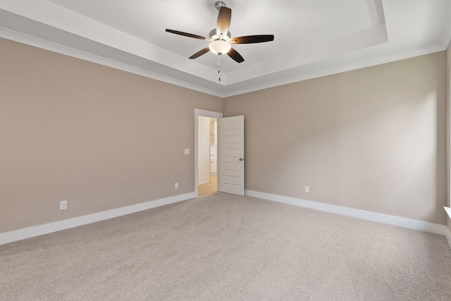 empty room with crown molding, a tray ceiling, light colored carpet, and ceiling fan