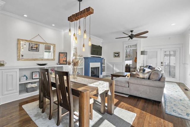 dining room with ceiling fan, a fireplace, ornamental molding, dark hardwood / wood-style flooring, and french doors