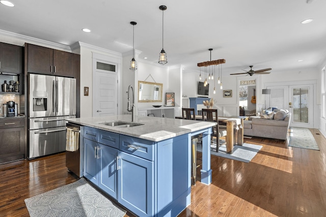 kitchen with sink, light stone counters, hanging light fixtures, stainless steel appliances, and a kitchen island with sink