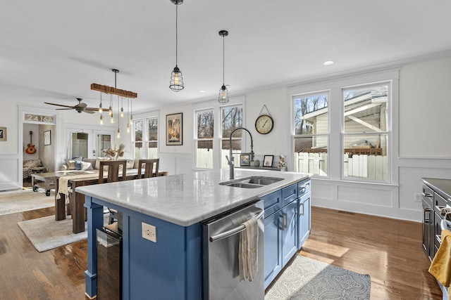 kitchen with pendant lighting, blue cabinets, an island with sink, sink, and stainless steel dishwasher