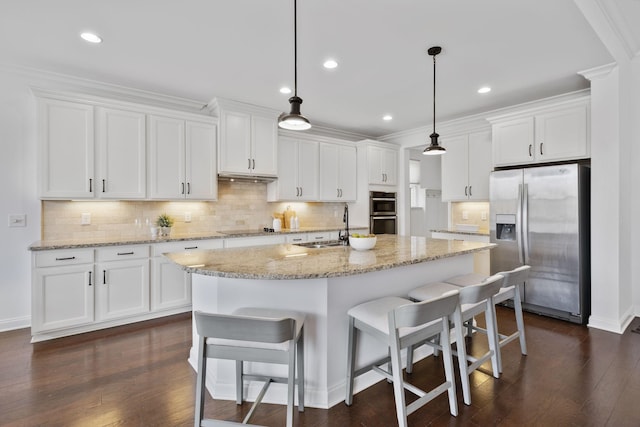 kitchen featuring appliances with stainless steel finishes, decorative light fixtures, white cabinetry, sink, and a kitchen island with sink