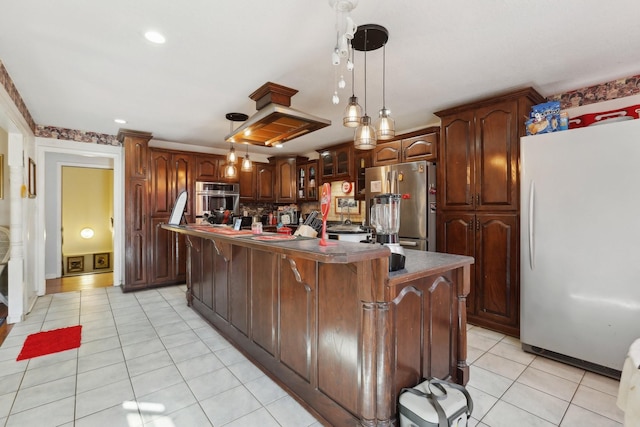 kitchen with appliances with stainless steel finishes, hanging light fixtures, a center island, light tile patterned floors, and dark brown cabinetry