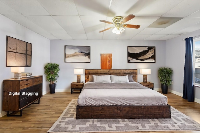 bedroom with wood finished floors, baseboards, and a drop ceiling