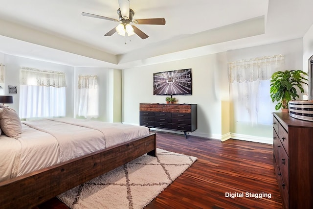 bedroom with dark wood finished floors, a raised ceiling, a ceiling fan, and baseboards