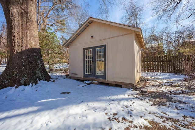 snow covered structure featuring an outbuilding and fence