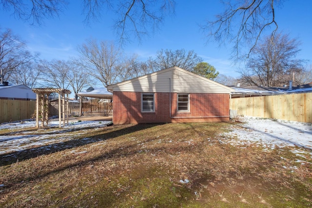 snow covered property with a carport, brick siding, a lawn, and a pergola