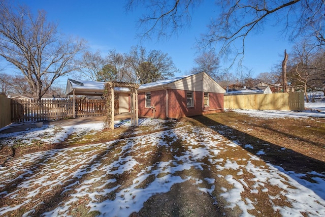 view of snow covered exterior featuring brick siding and fence