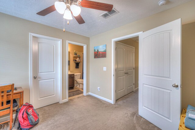 bedroom with ensuite bathroom, light colored carpet, ceiling fan, and a textured ceiling