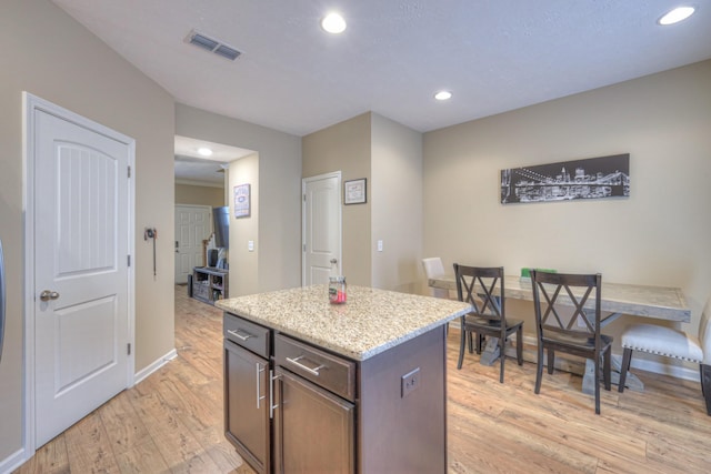 kitchen with dark brown cabinetry, light stone countertops, a kitchen island, and light wood-type flooring