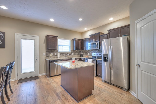 kitchen featuring light hardwood / wood-style flooring, dark brown cabinets, stainless steel appliances, tasteful backsplash, and a kitchen island