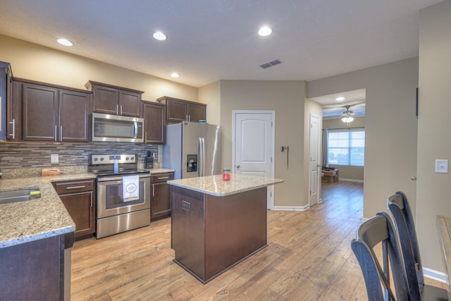 kitchen featuring appliances with stainless steel finishes, backsplash, light stone countertops, light hardwood / wood-style floors, and a kitchen island