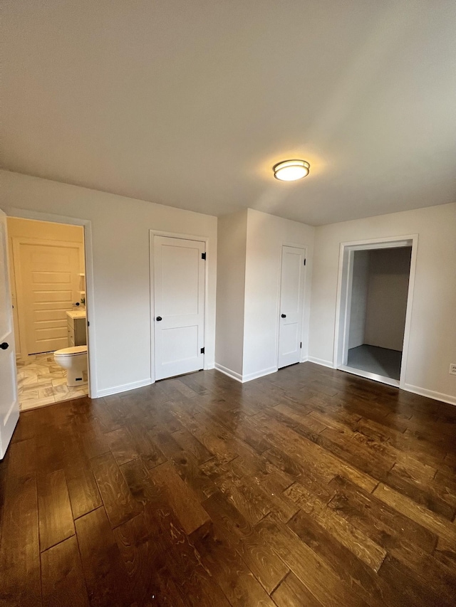 unfurnished bedroom featuring ensuite bath and dark hardwood / wood-style flooring