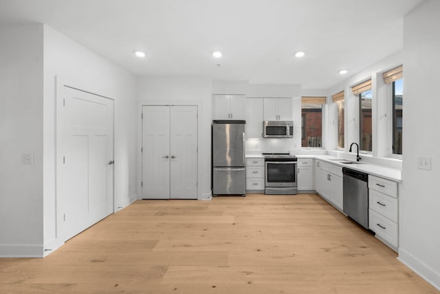 kitchen with white cabinetry, stainless steel appliances, sink, and light hardwood / wood-style flooring