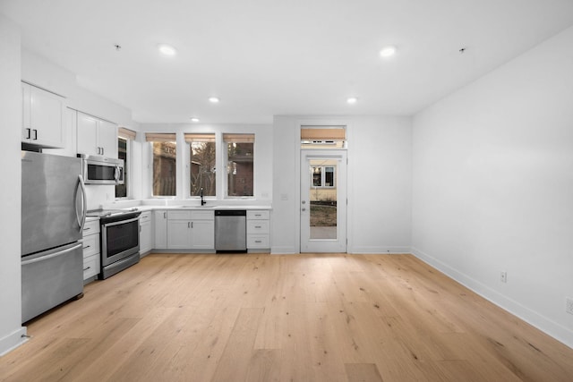 kitchen with appliances with stainless steel finishes, sink, white cabinets, and light hardwood / wood-style flooring