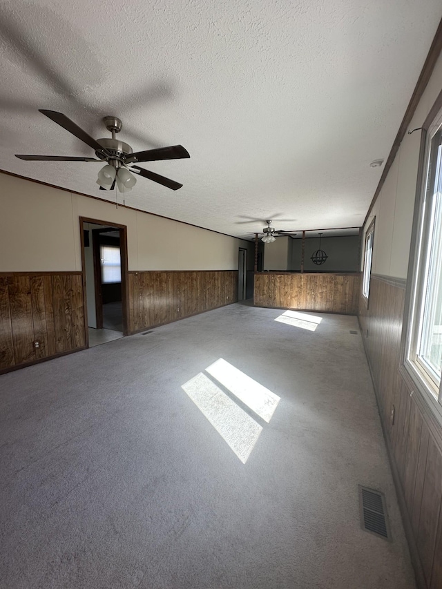 carpeted empty room featuring ceiling fan, wooden walls, and a textured ceiling