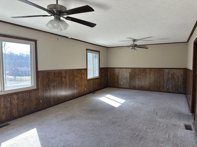 unfurnished room with wood walls, light colored carpet, ceiling fan, crown molding, and a textured ceiling